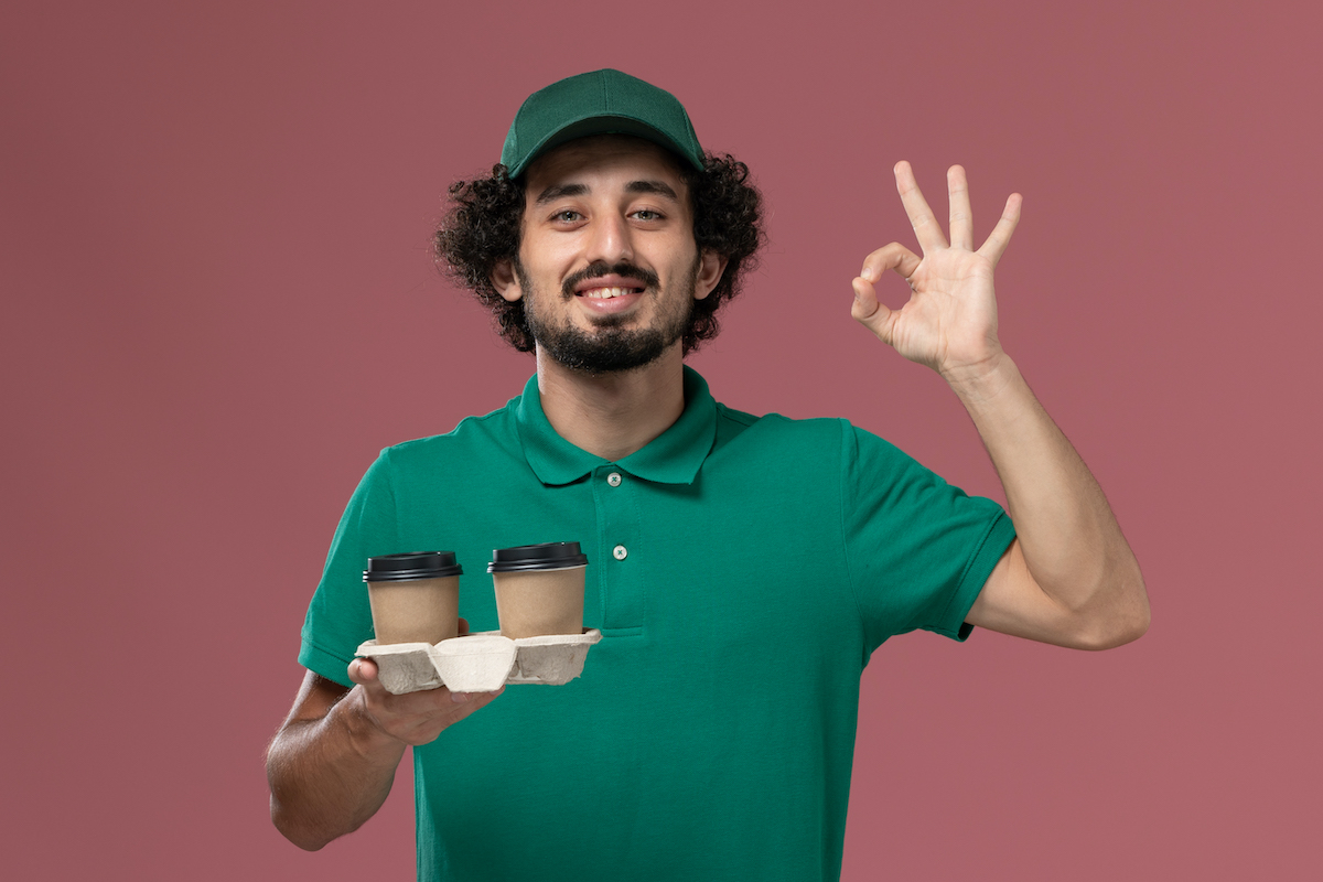 Front View Male Courier In Green Uniform And Cape Holding Coffee Cups On Pink Background Service Uniform Delivery Job Male