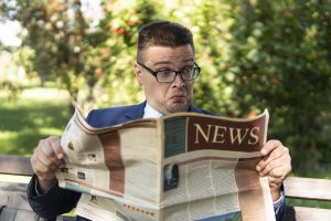 Successful Senior Businessman Reading A Financial Newspaper While Sitting In City Square, Outdoors. Emotion Of Surprise And Shock, Concept. Surprised Person Reads Fake News.